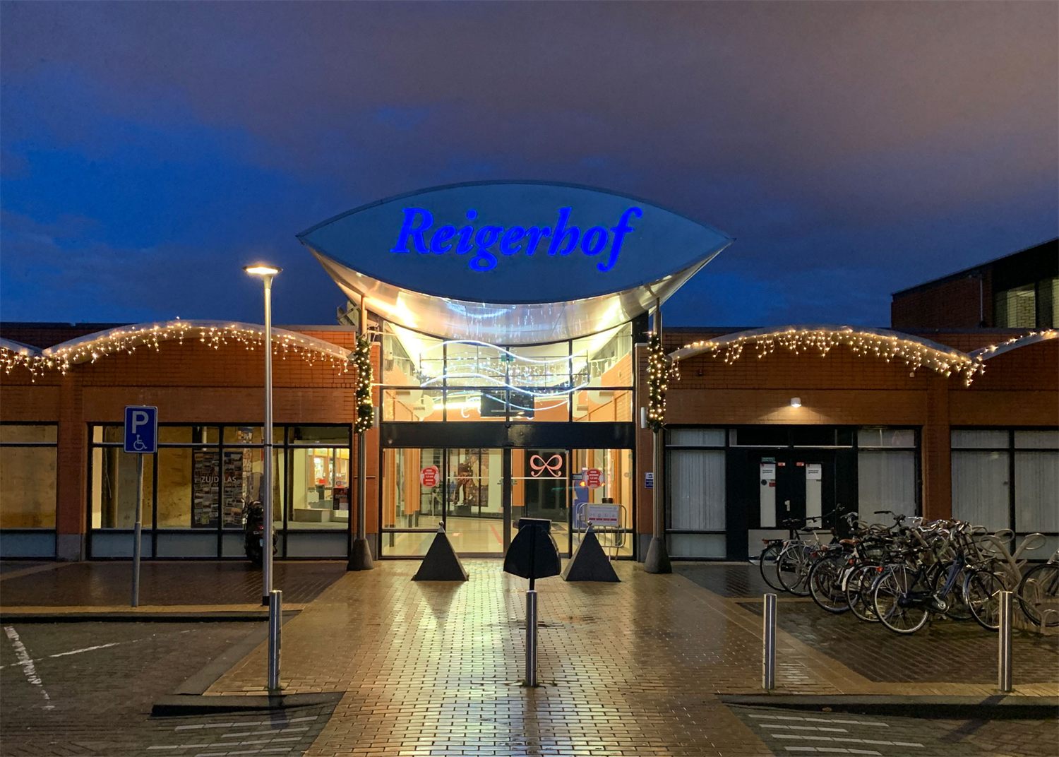 Gevel van winkelcentrum Reigerhof bij schemering met verlichte belettering en lichtlijnen