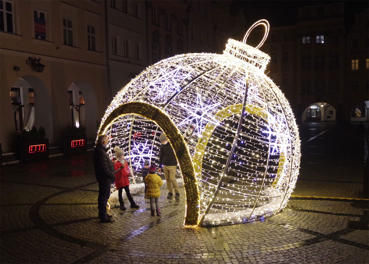Verlichte doorloopkerstbal op een stadsplein, bezoekers lopen er doorheen